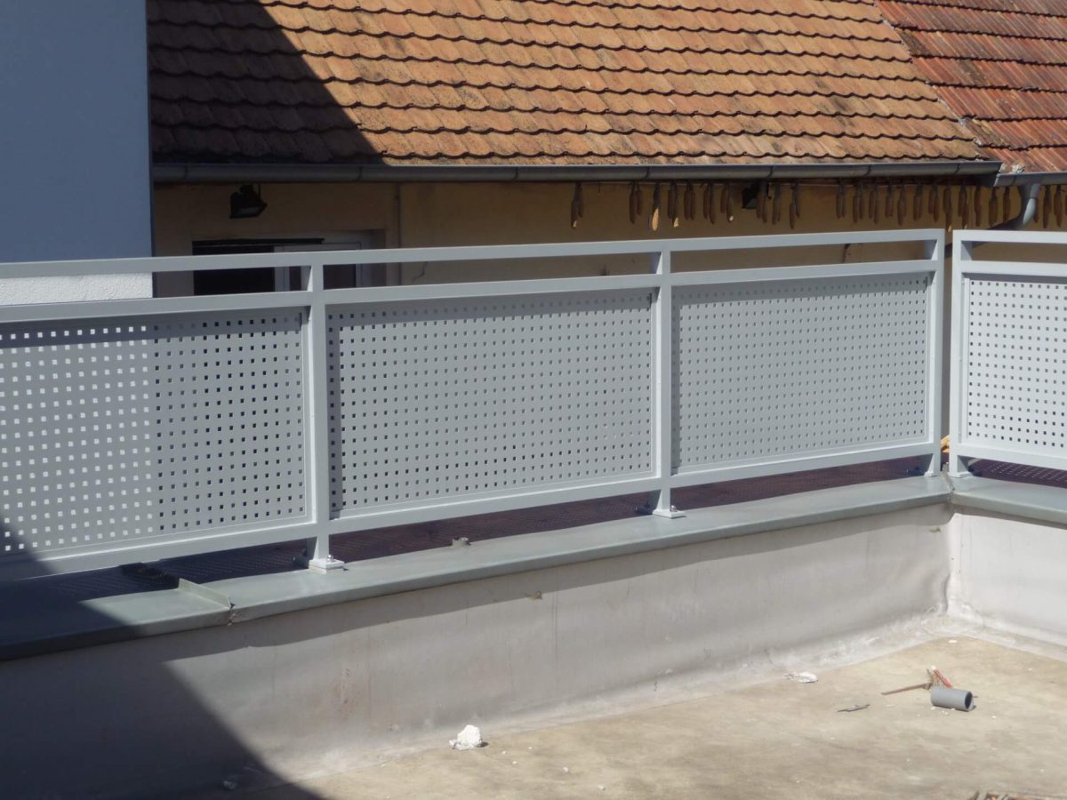Modernes Balkongeländer aus pulverbeschichtetem Aluminium mit Lochblechfüllung in hellem Grau, montiert auf einer gemauerten Brüstung