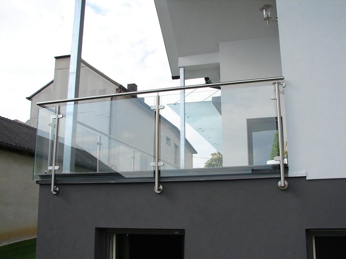 Modernes Balkongeländer aus Glas mit Edelstahlpfosten und Handlauf an einem weißen Wohnhaus