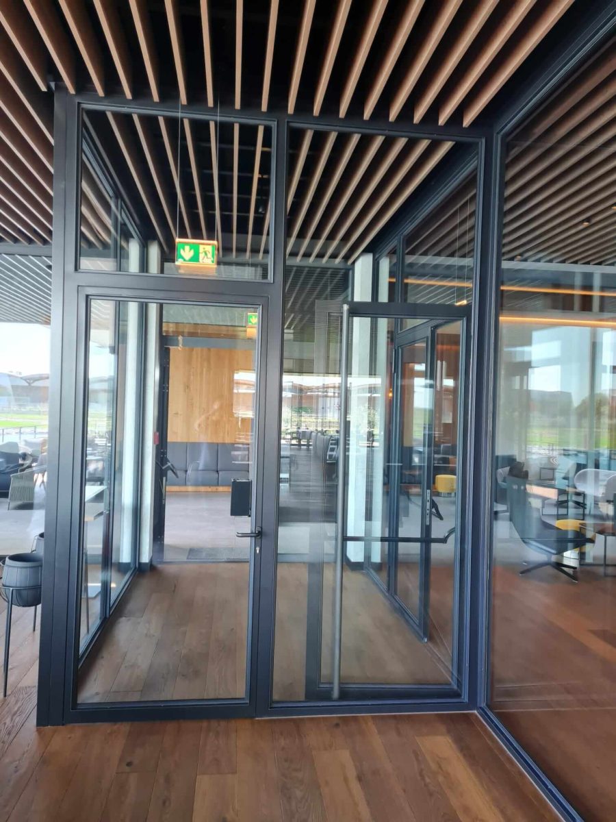 Moderne Fluchttür aus Glas mit schwarzem Aluminiumrahmen in einem Innenraum mit Holzdecke und Parkettboden