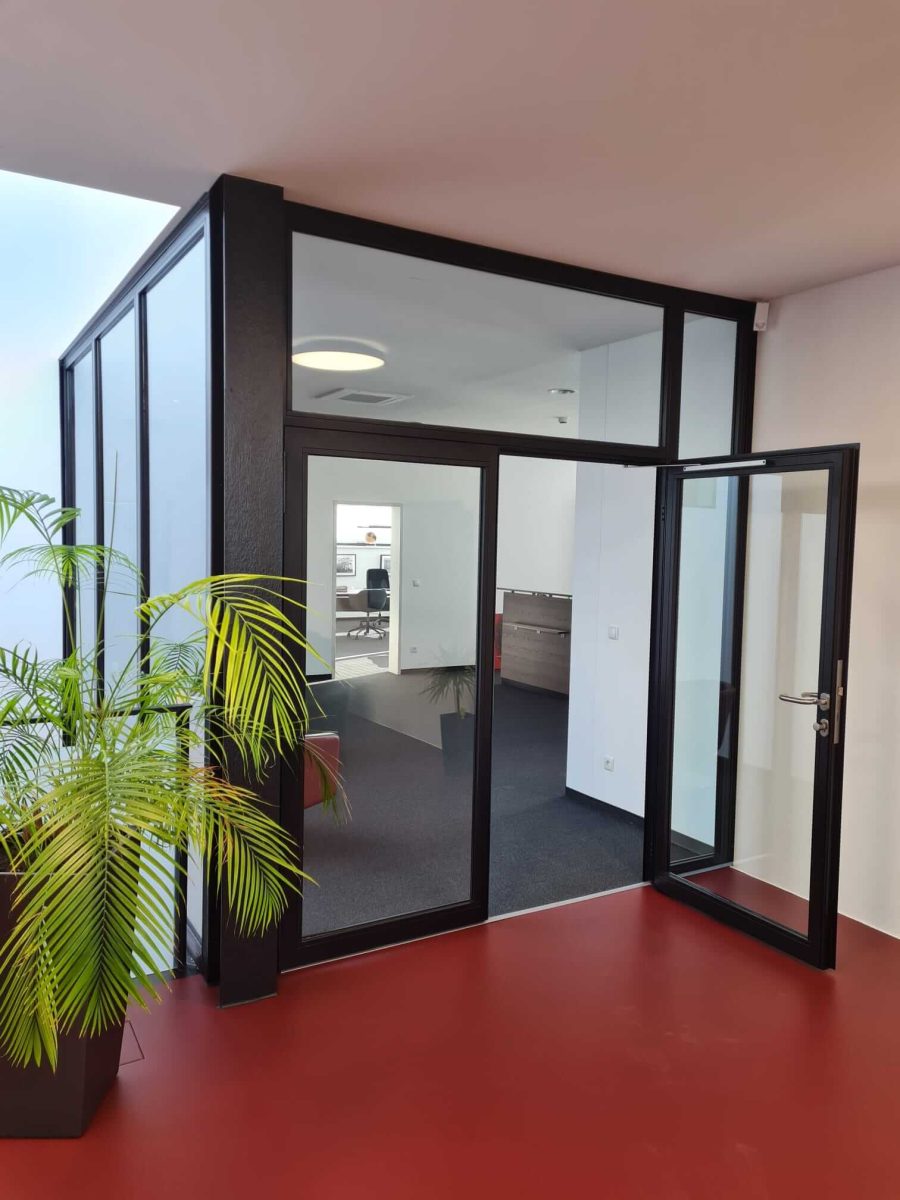 Moderne Glastrennwand mit schwarzem Rahmen und Türanlage in einem Bürogebäude mit rotem Boden