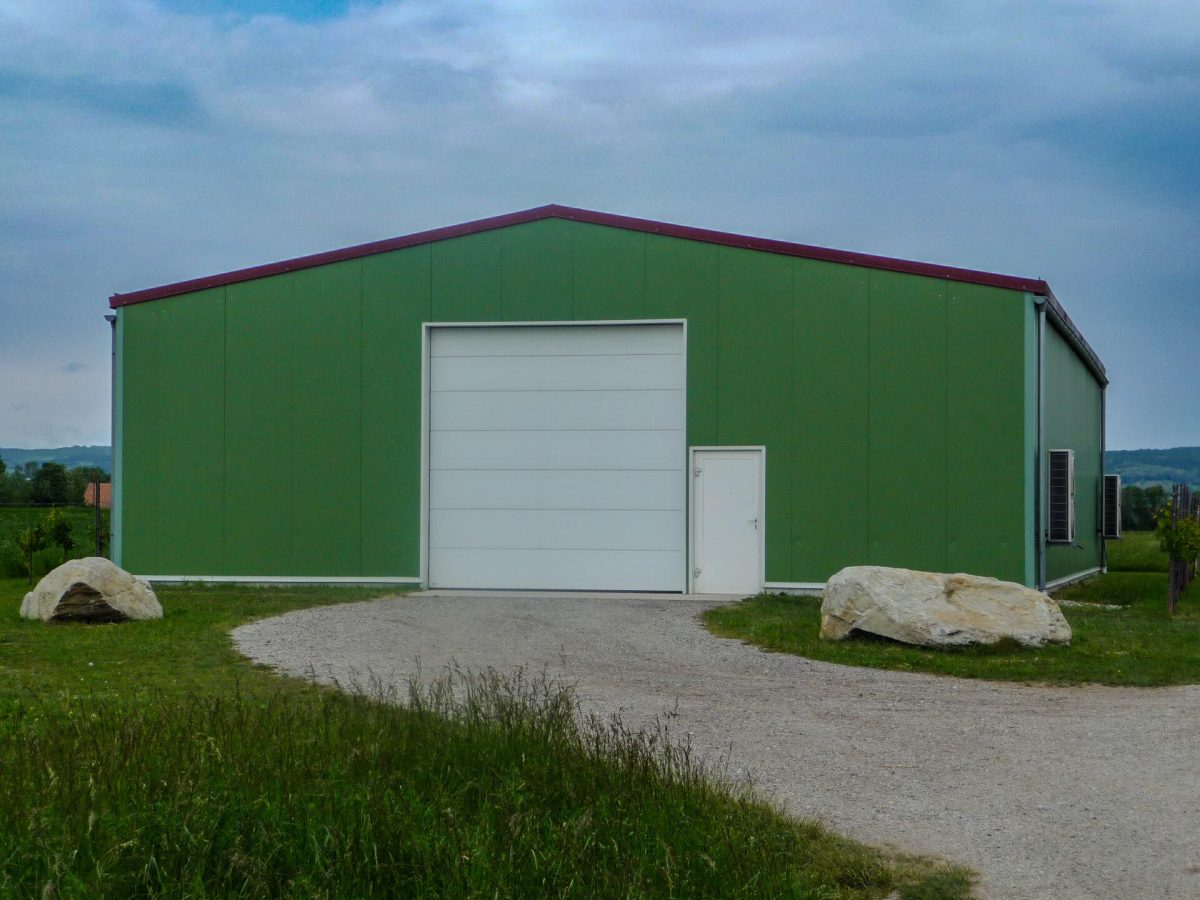 Geräumige Lagerhalle mit grünem Trapezblech, großem weißen Sektionaltor und separatem Zugang – ideal gelegen im ländlichen Raum.