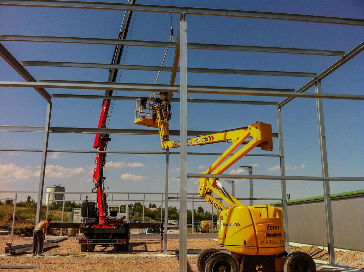 Montage einer Stahlkonstruktion für eine Industriehalle mit Hilfe von Hebebühne und Kran – professionelle Umsetzung durch Facharbeiter.