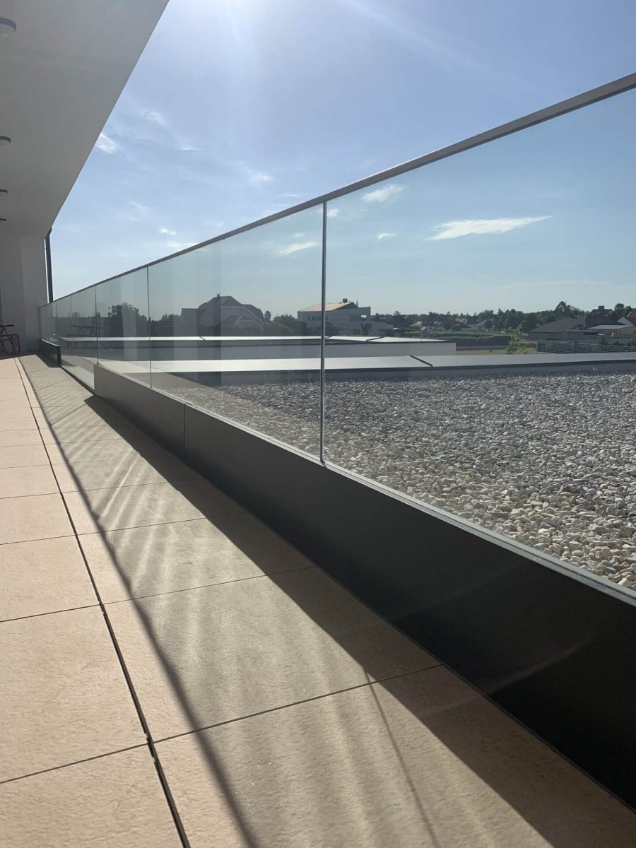 Modernes, rahmenloses Glasgeländer auf einem Balkon mit Ausblick über ein Wohngebiet bei Sonnenschein