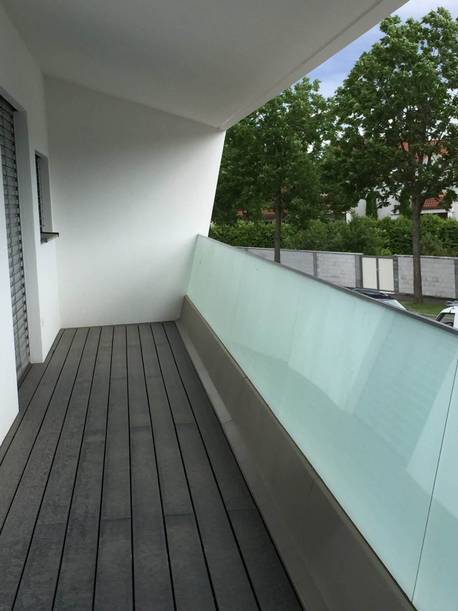 Modernes Balkongeländer aus satiniertem Glas in einem minimalistischen Wohngebäude mit dunklem Bodenbelag