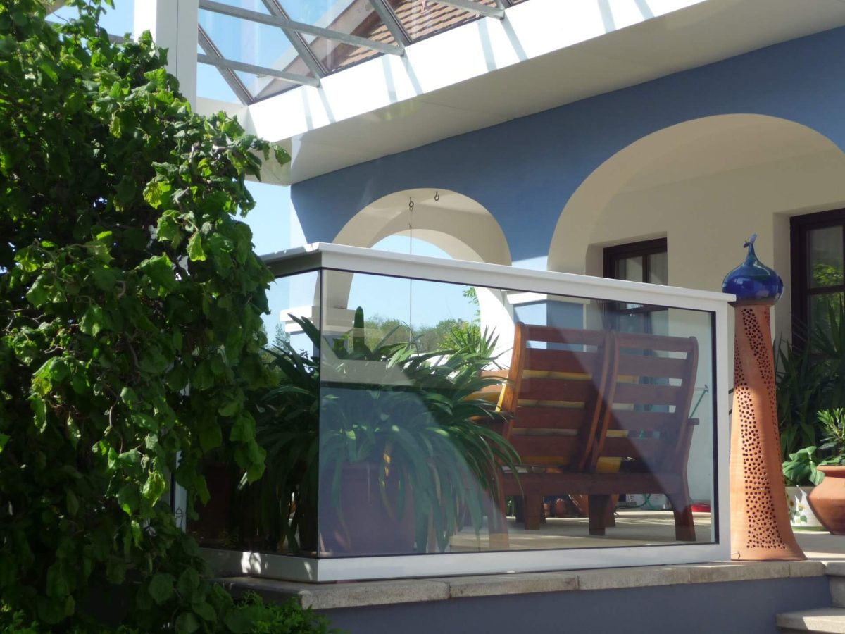 Modernes Glasgeländer mit weißem Rahmen auf einer mediterranen Terrasse mit Sitzbank und Pflanzen