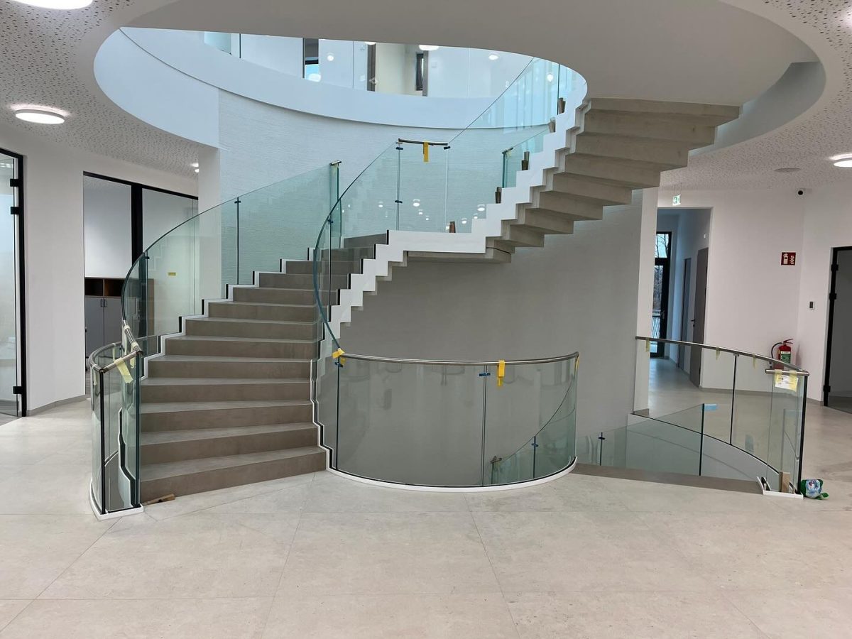 Großzügige, moderne Treppenanlage mit Glasbrüstung und geschwungener Form in einem lichtdurchfluteten Innenbereich