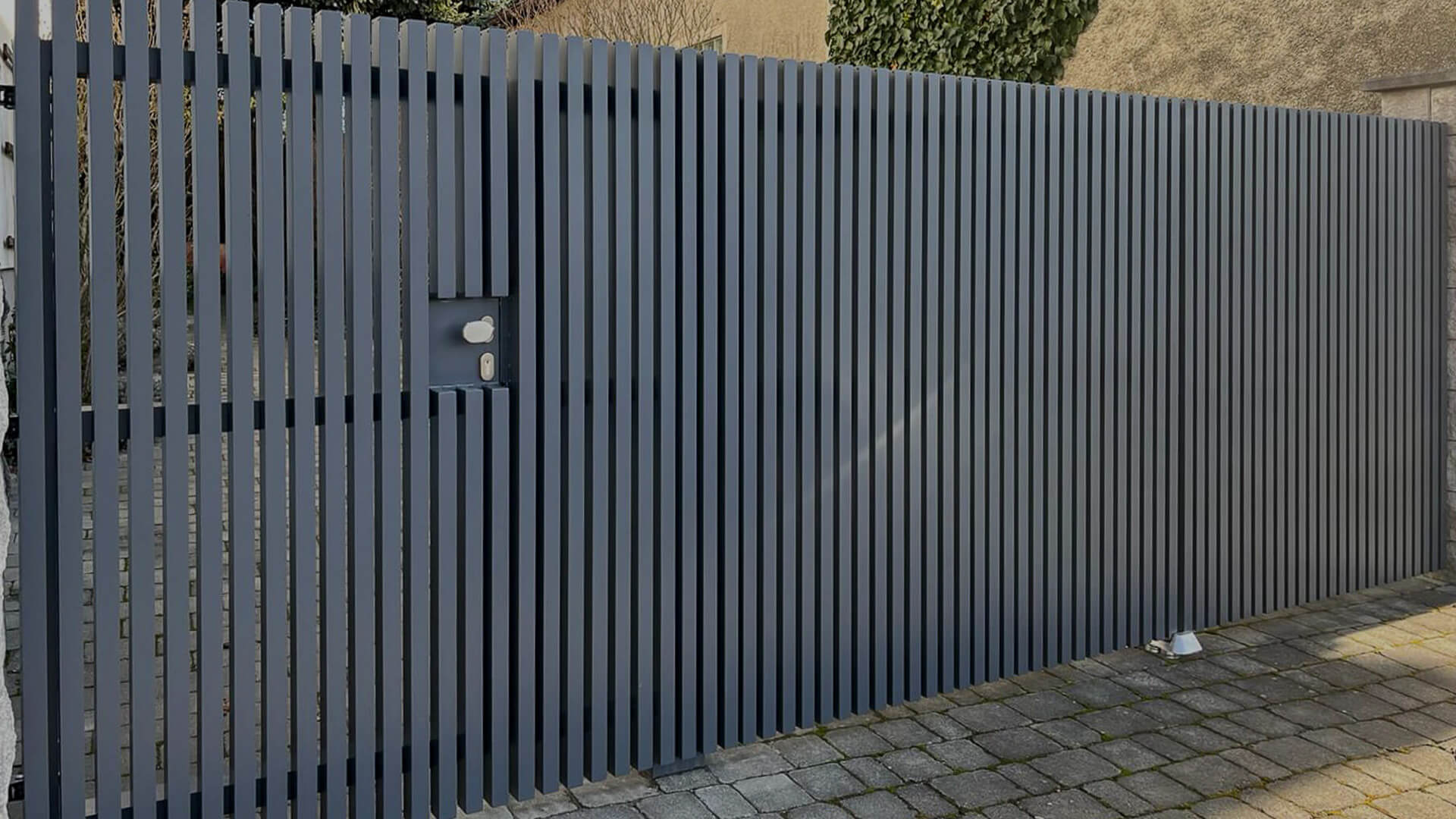 Moderner Sichtschutzzaun aus vertikalen Aluminiumlamellen in Anthrazitgrau mit integrierter Tür und Schloss