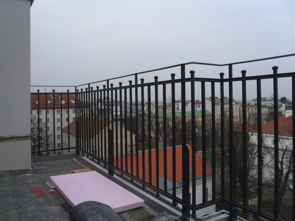 Klassisches, pulverbeschichtetes Stahlgeländer mit senkrechten Füllstäben und Zierkugeln – ideal für den Einsatz auf Dachterrassen mit urbanem Ausblick