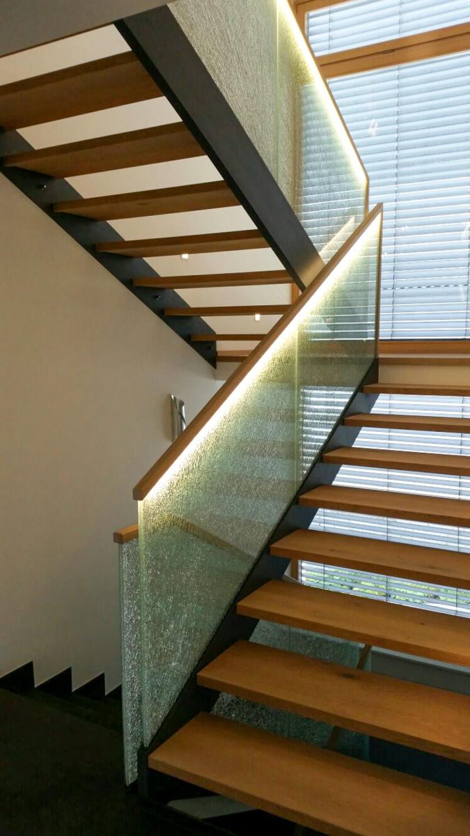 Moderne Treppenkonstruktion mit freitragenden Holzstufen, seitlich getragen von Stahlwangen, kombiniert mit satiniertem Glasgeländer und integrierter LED-Beleuchtung