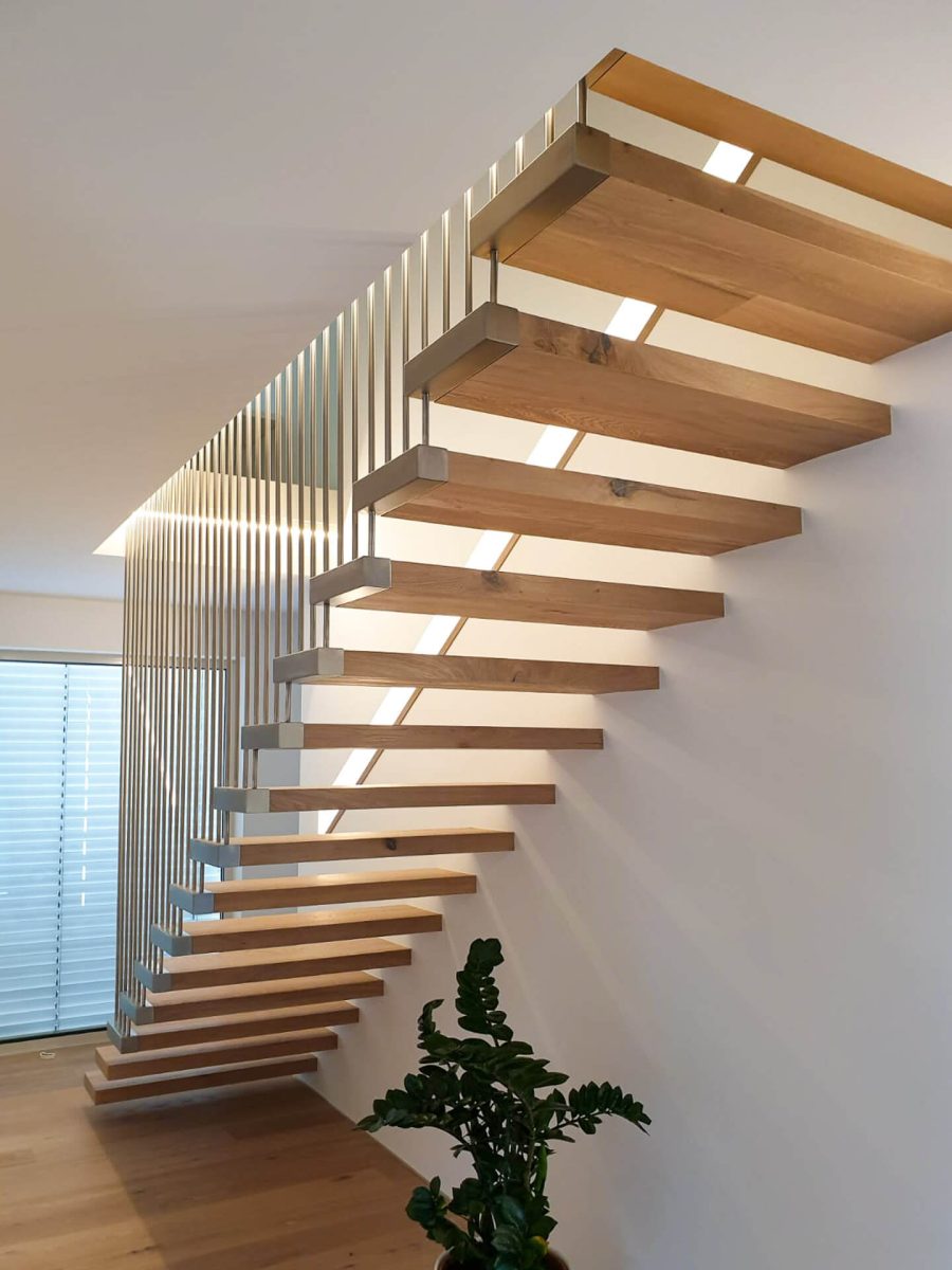 Minimalistische freitragende Treppe mit massiven Eichenstufen, seitlicher Aufhängung durch vertikale Edelstahlstäbe und integrierter LED-Wandbeleuchtung