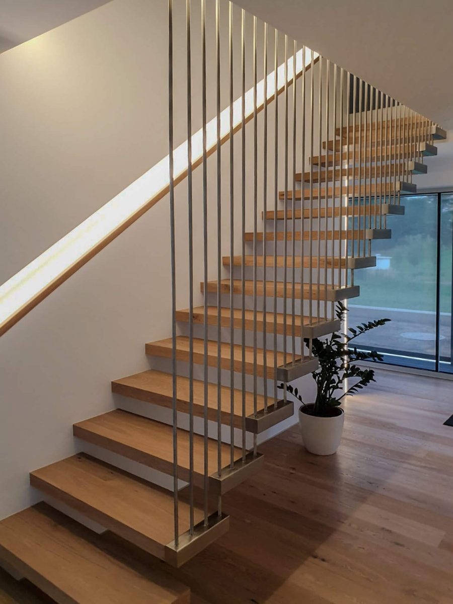 Elegante freitragende Treppe mit massiven Holzstufen und senkrechten Metallstäben als Geländer, kombiniert mit indirekter Wandbeleuchtung in einem modernen Wohnambiente