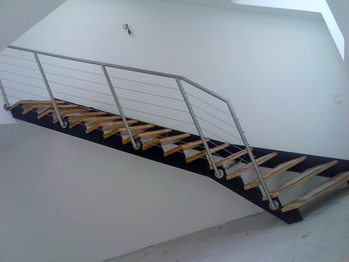 Moderne Innentreppe mit offenen Holzstufen auf dunkler Stahlwange und seitlichem Edelstahlgeländer mit horizontalen Seilen, eingebaut in einen hellen, minimalistischen Raum
