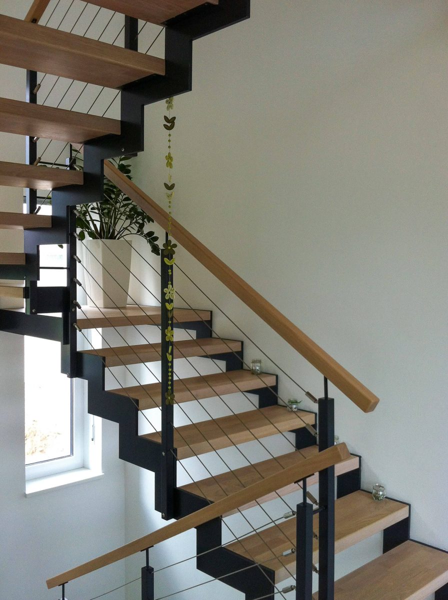 Moderne Innentreppe mit offenem Design, Holzstufen auf schwarzer Stahlkonstruktion und seitlichem Seilgeländer, kombiniert mit einem Holzhandlauf in heller Wohnumgebung