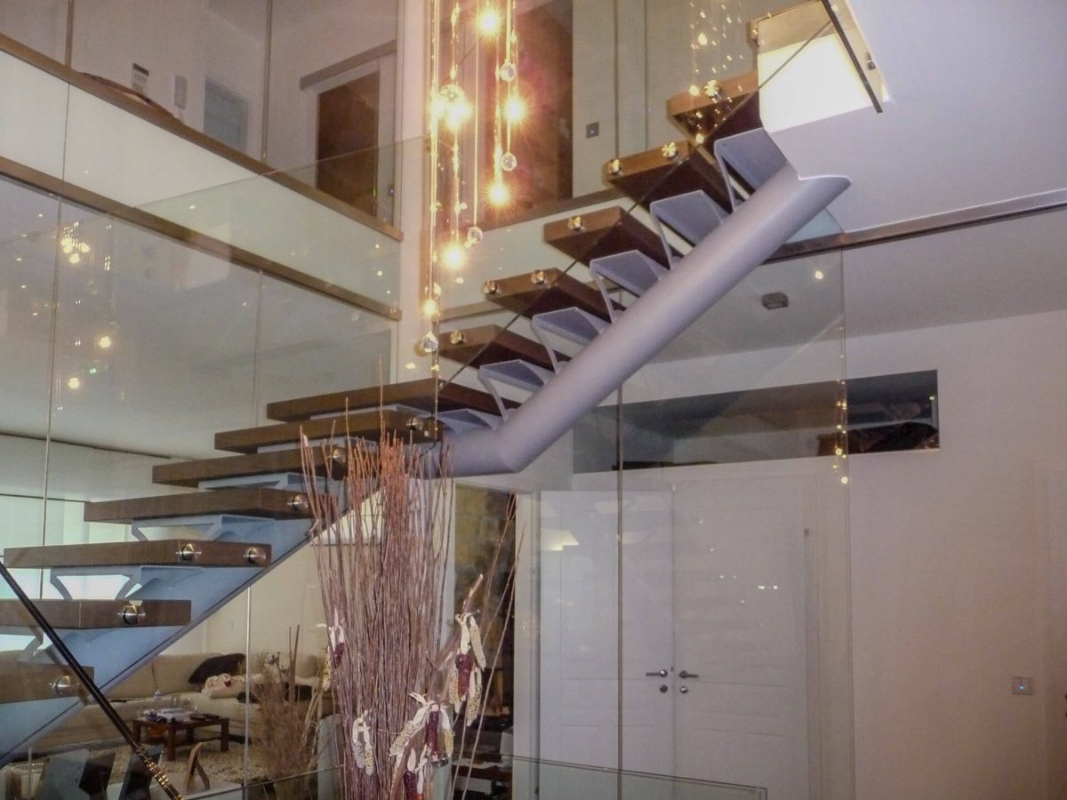 Moderne freitragende Treppe mit dunkelbraunen Holzstufen auf einer mittigen Stahlwange, umgeben von Glasgeländern und stilvoller Beleuchtung in einem eleganten Wohnraum