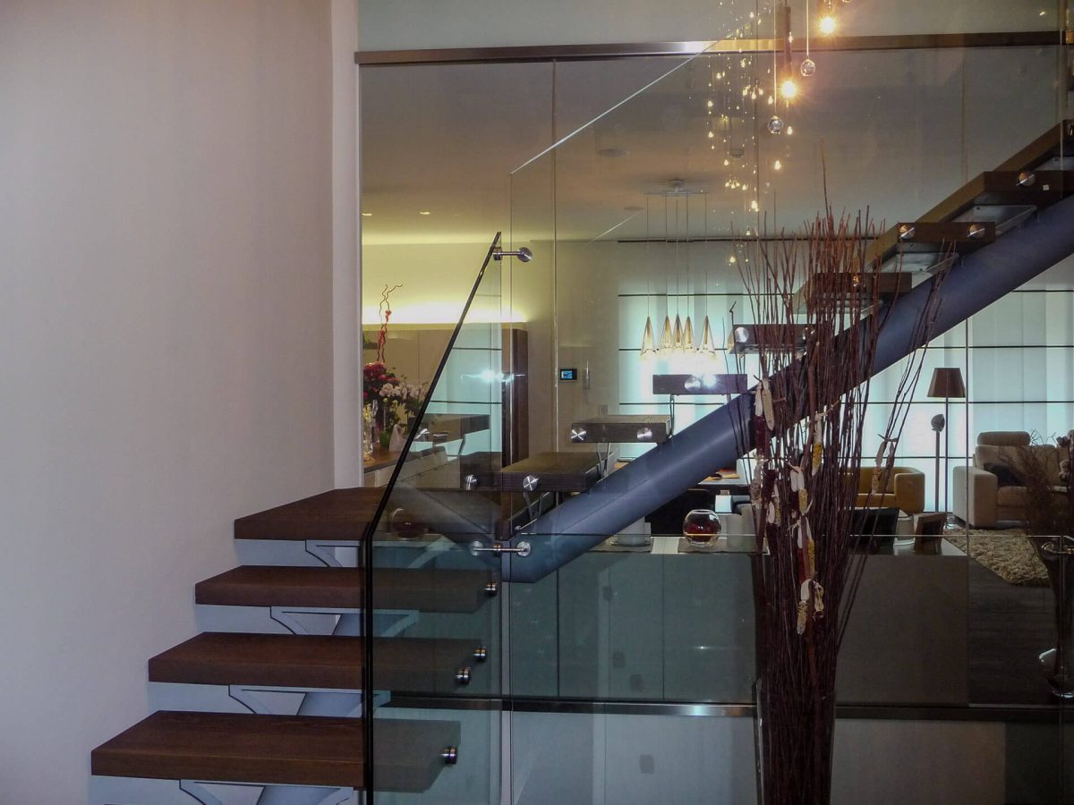 Moderne Treppenkonstruktion mit freitragenden Holzstufen und durchgehendem Glasgeländer in einem stilvoll eingerichteten Wohnbereich.
