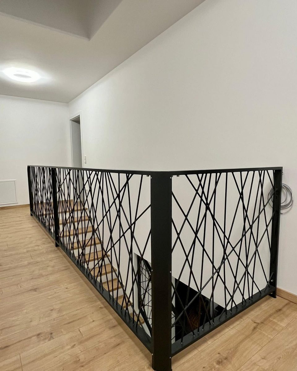 Innenliegendes Treppengeländer aus schwarzem Stahl mit unregelmäßig gekreuzten Streben in modernem Design, montiert auf hellem Holzboden in einem Wohnhaus