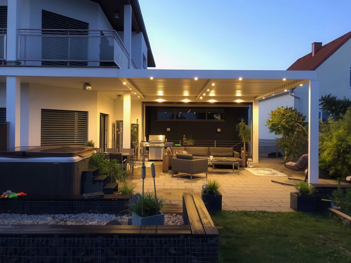 Abendlich beleuchtete Terrassenüberdachung mit integriertem Lichtsystem, Lounge-Bereich und Whirlpool im modernen Gartenambiente.