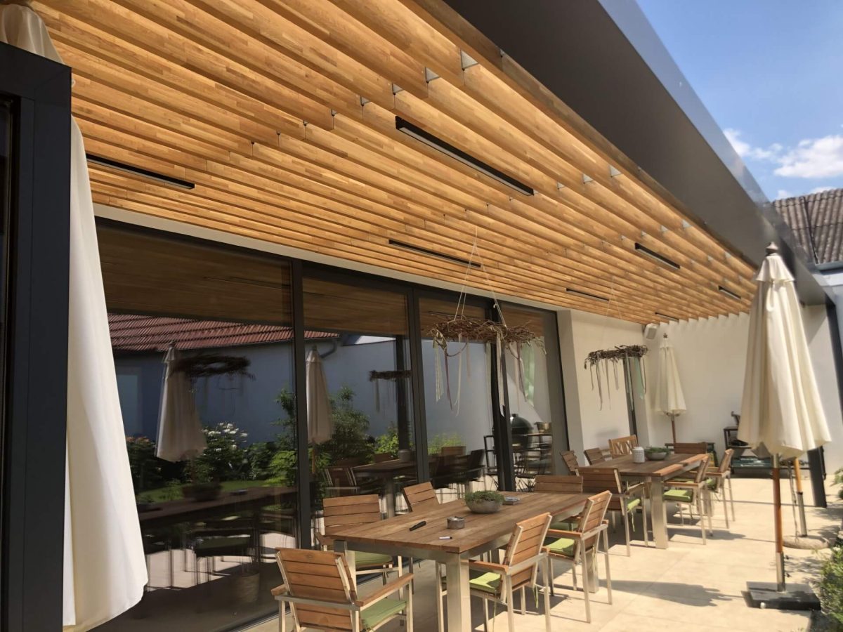 Überdachte Terrasse mit modernen Holzelementen an der Decke, ausgestattet mit Sitzgruppen und stimmungsvoller Beleuchtung für gemütliche Aufenthalte im Freien.