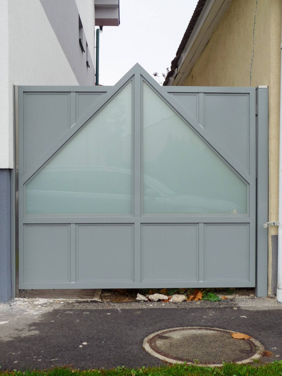Modernes Aluminiumtor in hellem Grau mit dekorativem Dreiecksgiebel und großflächigen Milchglaseinsätzen, eingebaut zwischen zwei Gebäuden als Sichtschutzlösung