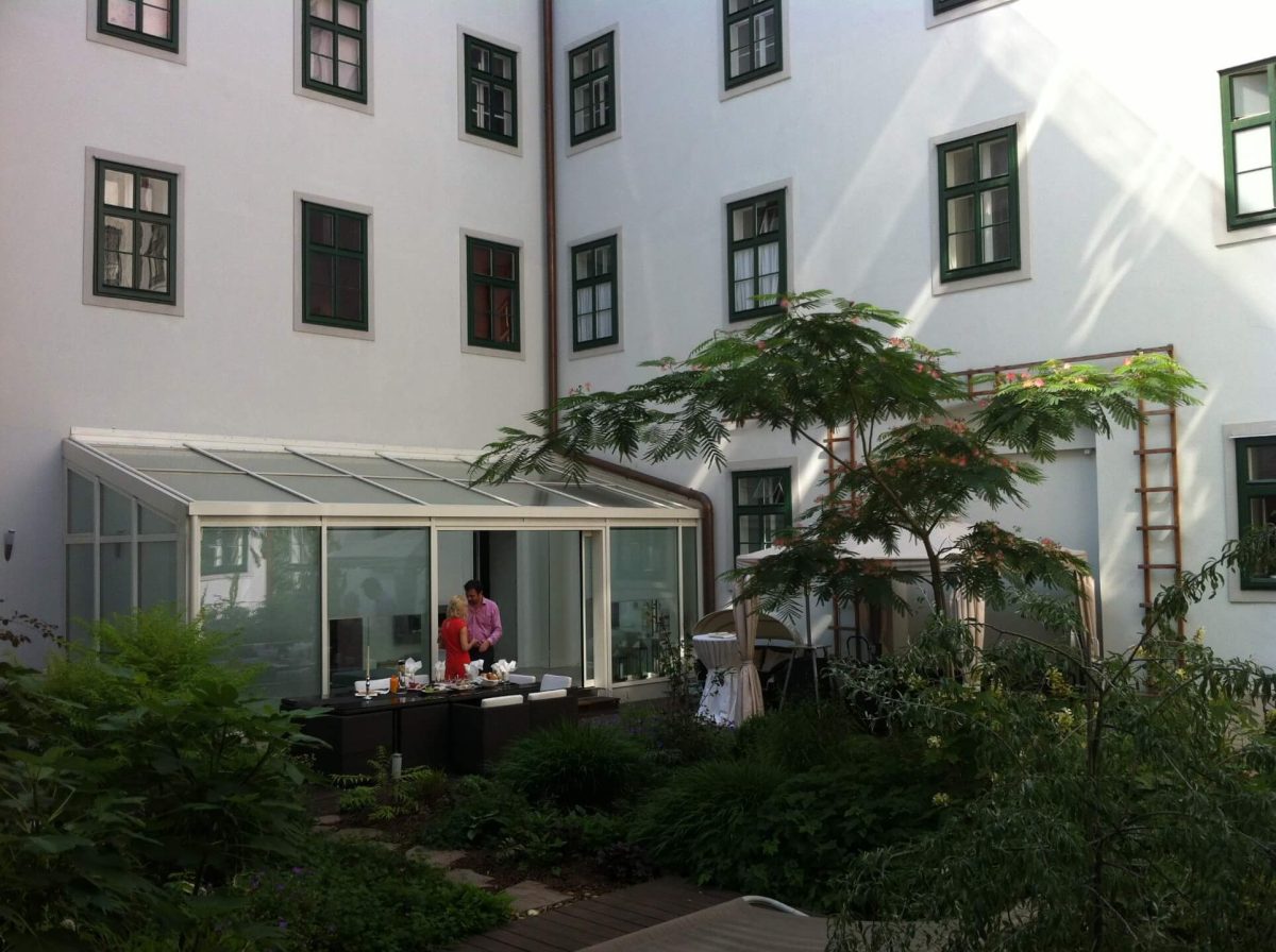 Moderner Wintergarten mit Glasdach in einem begrünten Innenhof, ideal für geschützten Aufenthalt im Freien bei jeder Witterung.