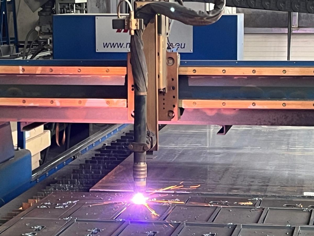 Nahaufnahme eines Plasmaschneidkopfs im Einsatz, Funkenflug und Lichtbogen während des Zuschnitts einer Metallplatte