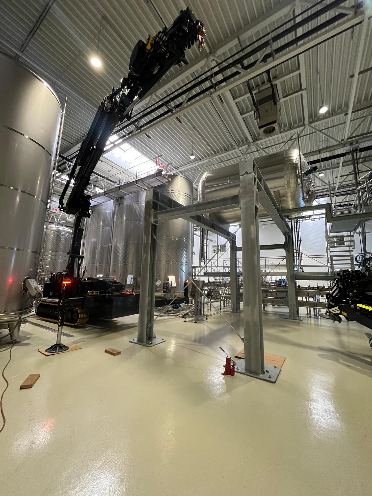 Montage einer großen Stahlbaukonstruktion mit Hilfe eines Ladekrans zwischen Edelstahlbehältern in moderner Industriehalle
