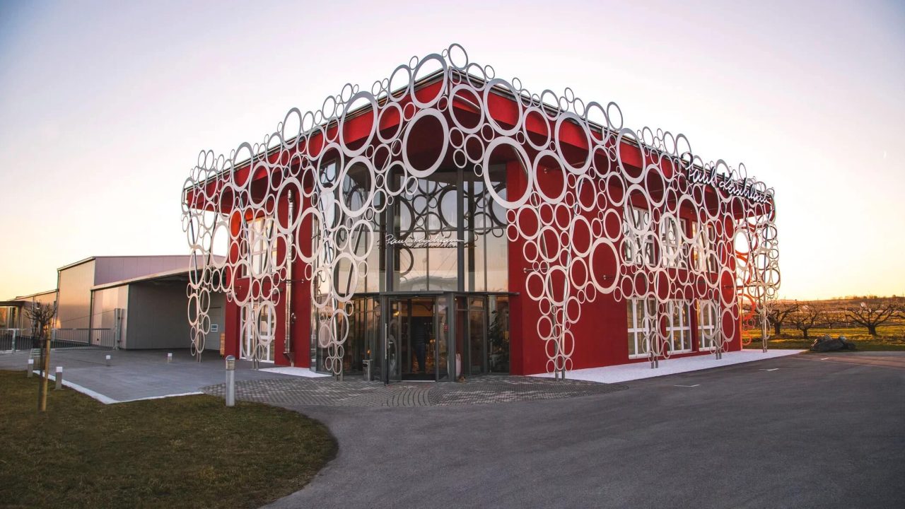 Ein modernes rotes Gebäude mit einer auffälligen, dekorativen Metallfassade aus ineinander verschlungenen Ringen in verschiedenen Größen.