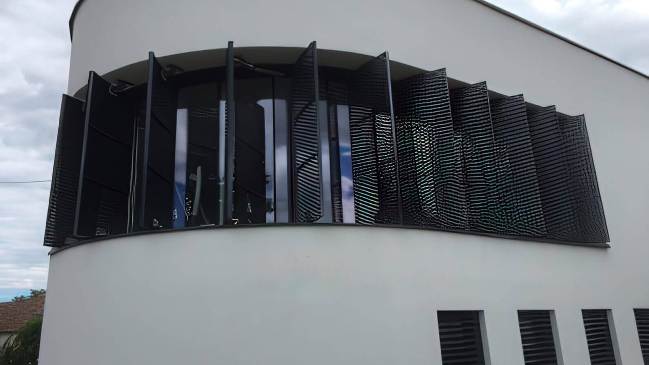 Gebogene Fassade mit vertikal angebrachten, beweglichen Metalllamellen zur Beschattung und Gestaltung eines modernen Gebäudes
