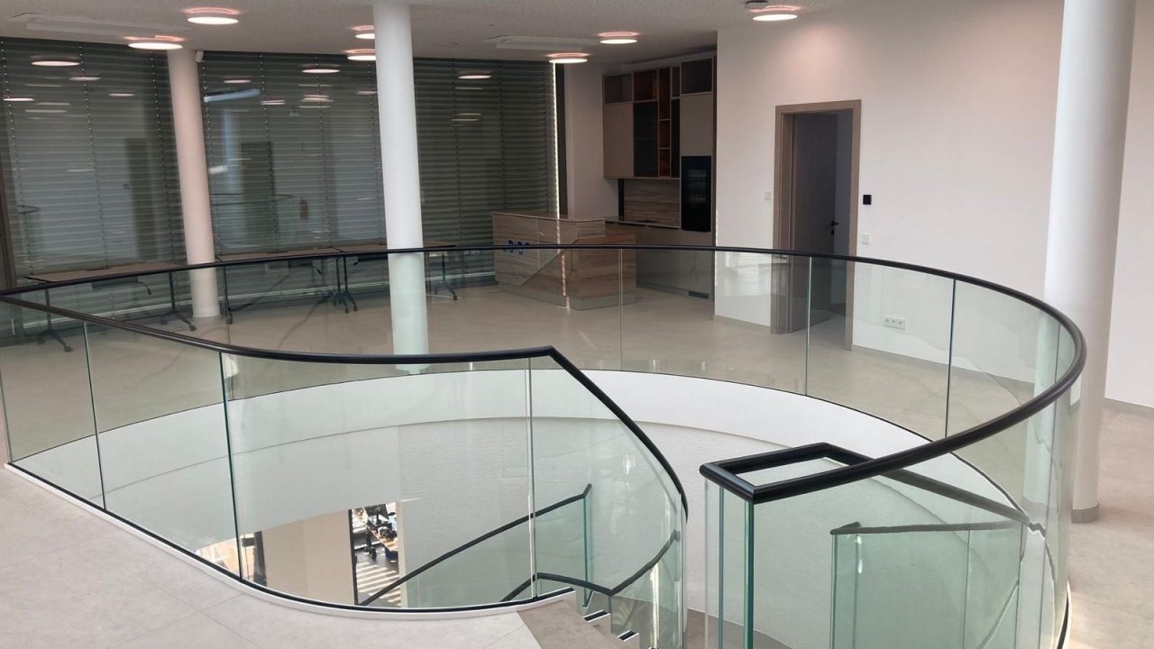 Runde Treppenöffnung mit elegantem Glasgeländer und schwarzem Handlauf in einem lichtdurchfluteten Innenraum