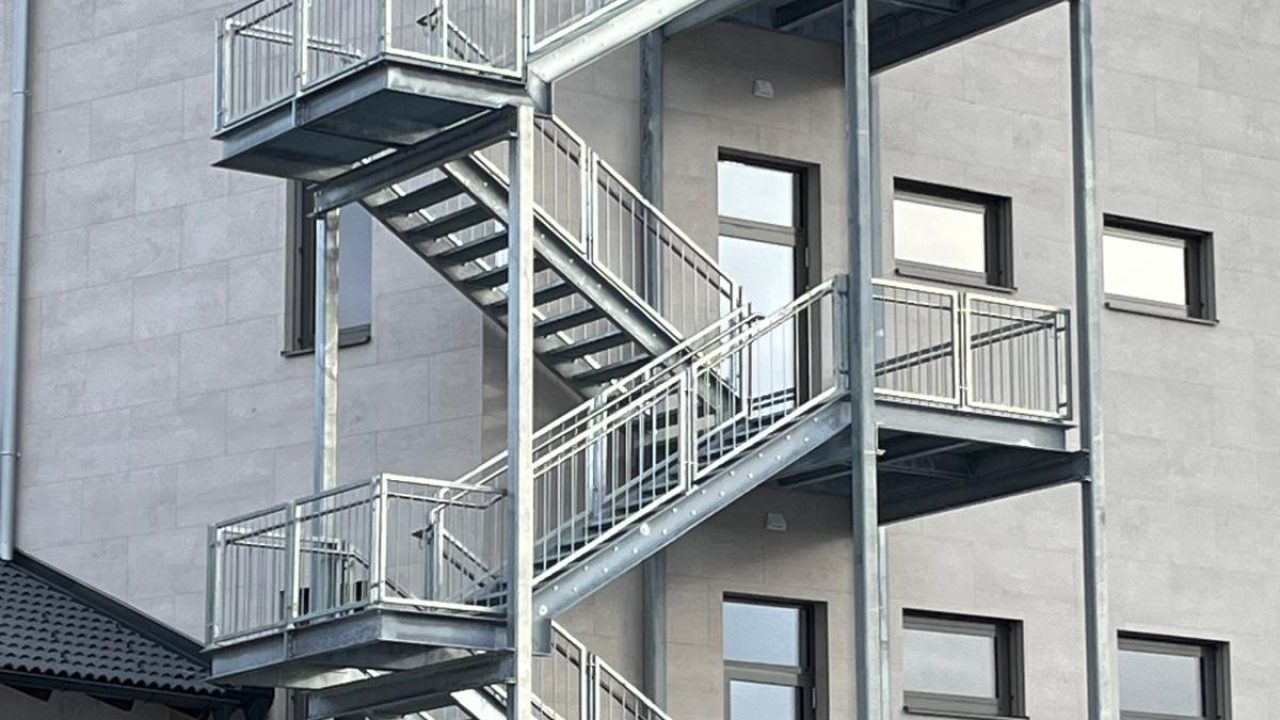Mehrstöckige verzinkte Stahltreppe mit Podesten und Geländer an der Fassade eines modernen Bürogebäudes