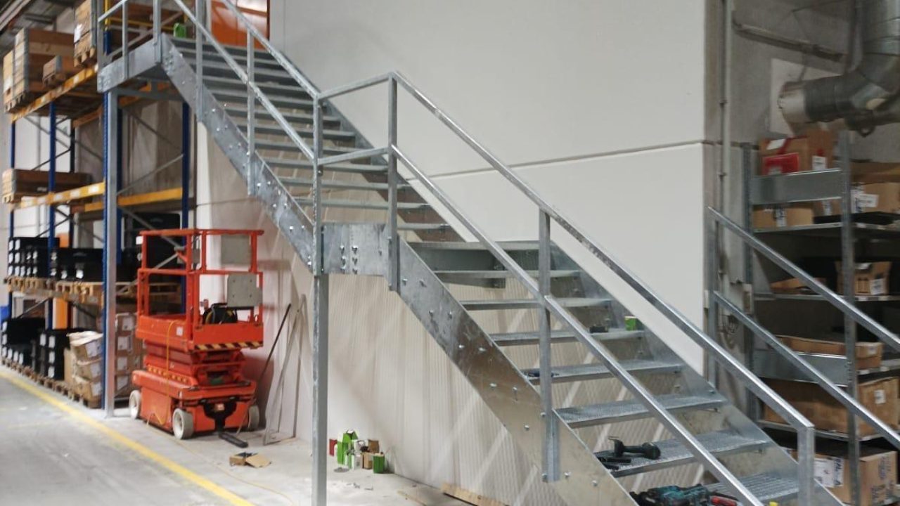 Feuerverzinkte Metalltreppe mit Gitterroststufen und Handlauf, montiert an der Wand einer Industriehalle