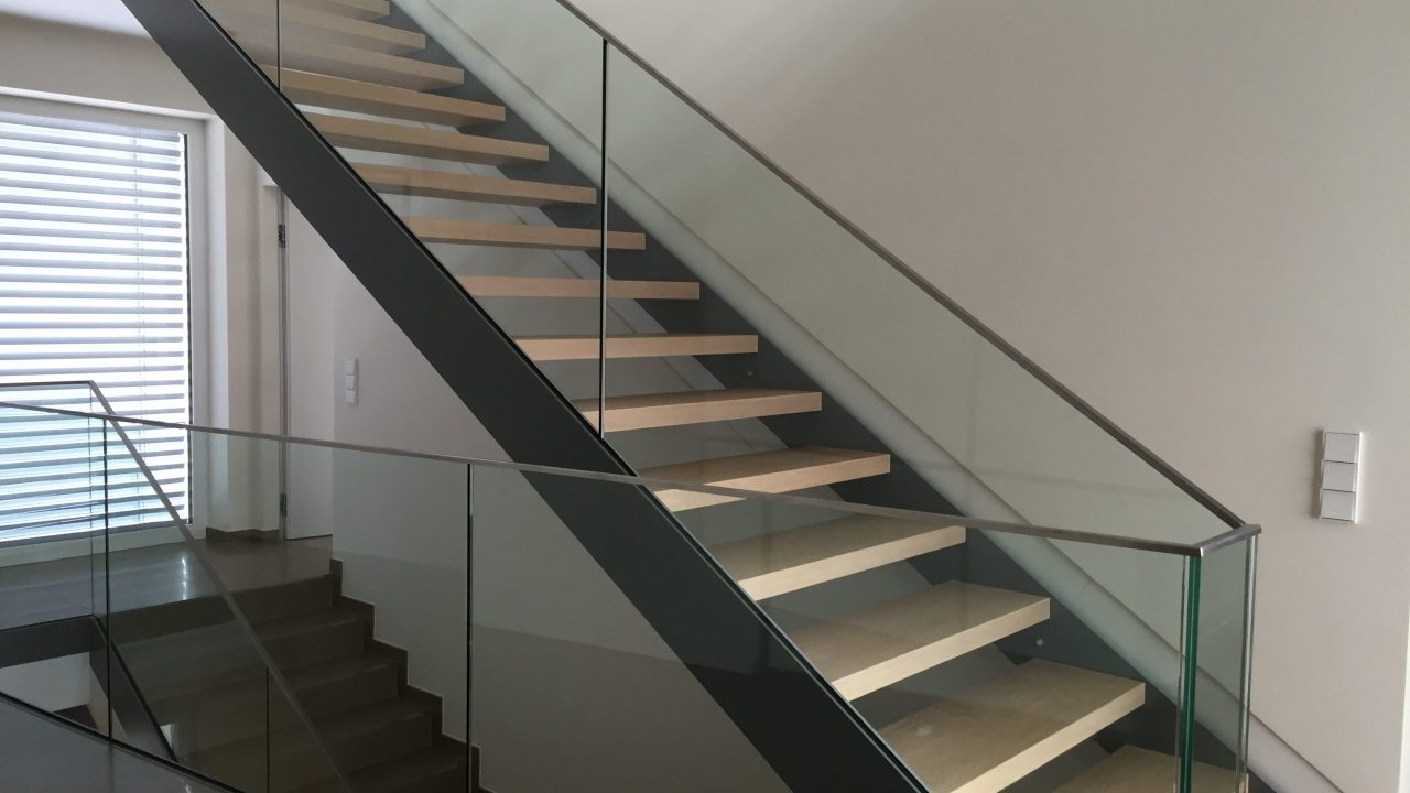 Moderne Innentreppe mit hellen Holzstufen und seitlichem Geländer aus klarem Sicherheitsglas