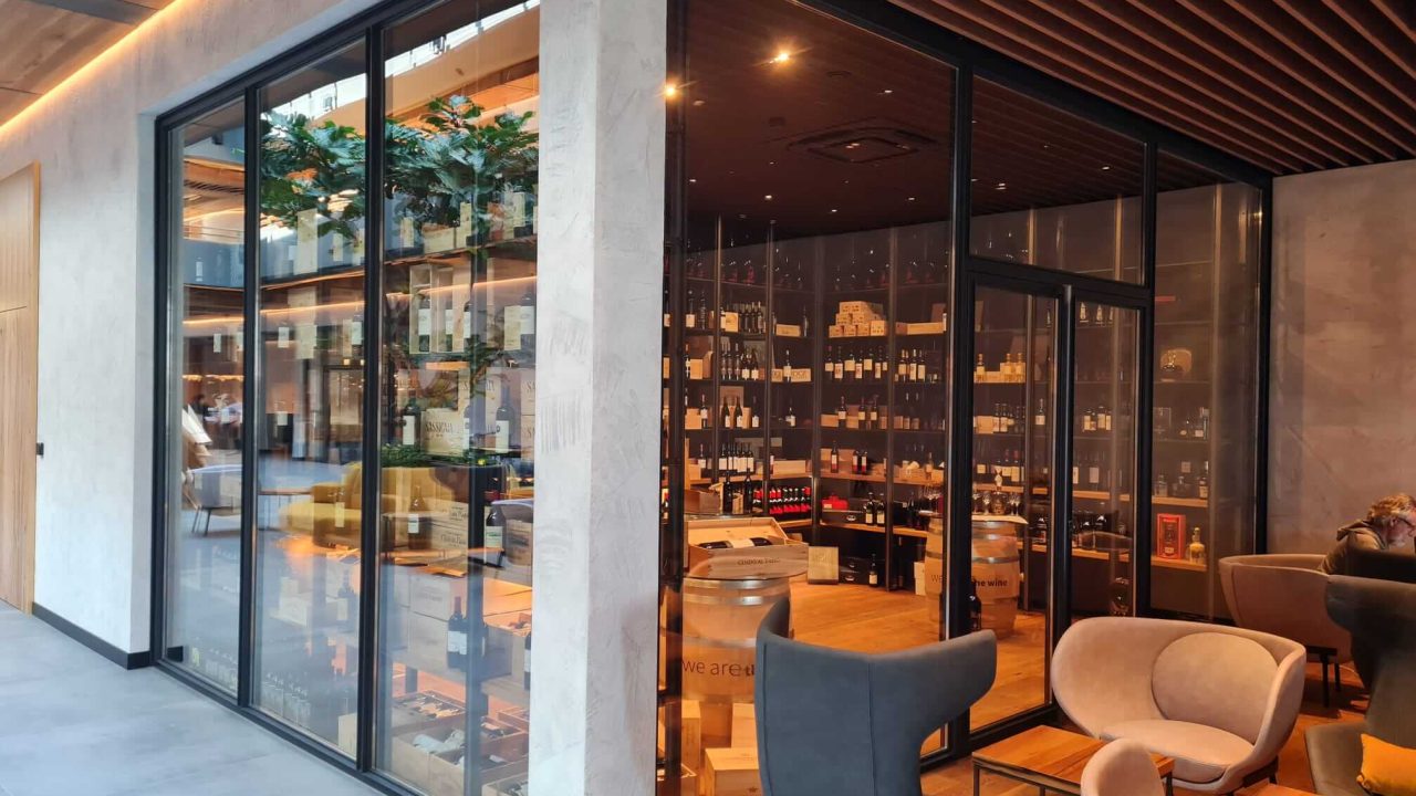 Moderne Weinlounge mit gemütlichen Sitzgelegenheiten und abgetrenntem Weinlager hinter einer großflächigen Glaswand