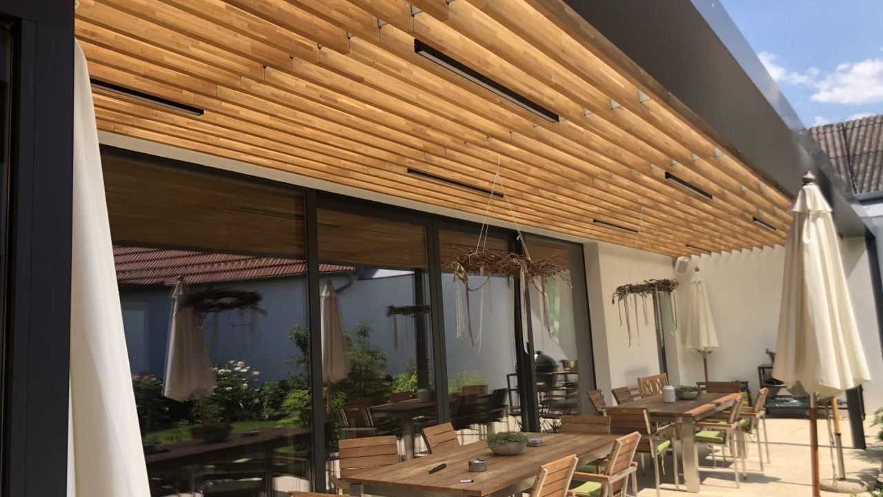 Überdachte Terrasse mit modernen Holzelementen an der Decke, ausgestattet mit Sitzgruppen und stimmungsvoller Beleuchtung für gemütliche Aufenthalte im Freien.