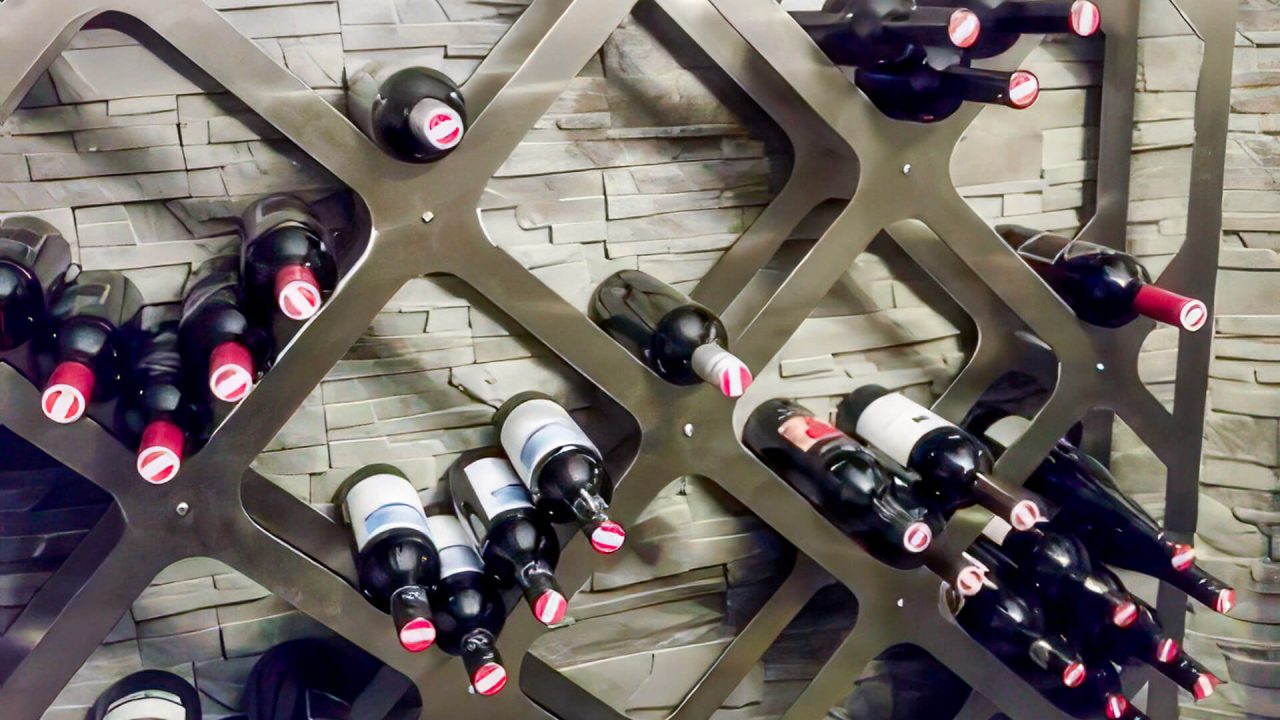 Modernes Weinregal aus Metall mit schräg angeordneten Halterungen für Weinflaschen, montiert vor einer Wandverkleidung aus Naturstein.